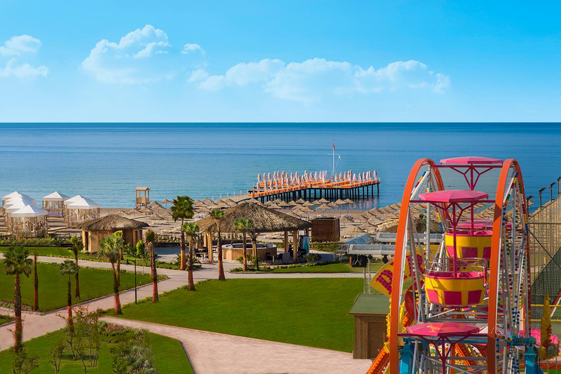 Außenansicht des Aska Lara Resort & Spa mit Blick auf den Strand, Pier und Fahrgeschäft.