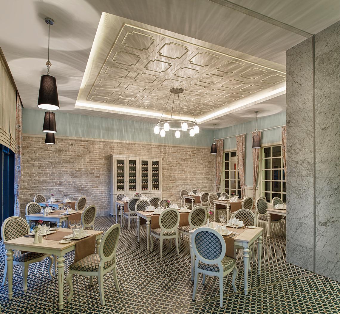 Innenansicht des Restaurants im Aska Lara Resort & Spa mit Tisch, Stühlen und dekorativen Deckenleuchten.