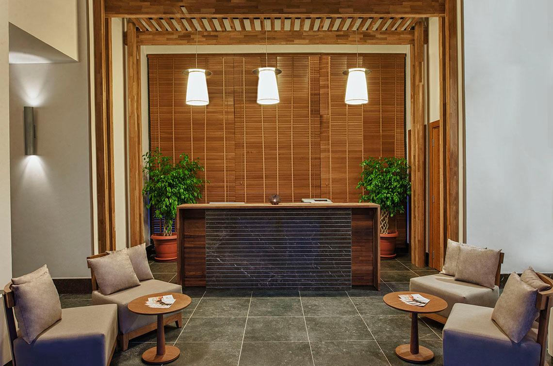 Empfangsbereich des Aska Lara Resort & Spa mit Holzwänden, gepolsterten Sesseln und einem Empfangstresen.