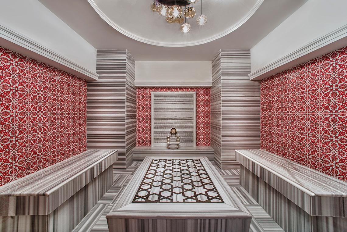 Innenbereich eines Spas im Aska Lara Resort & Spa mit roten und grauen Wandfliesen und einer zentralen Liegefläche.