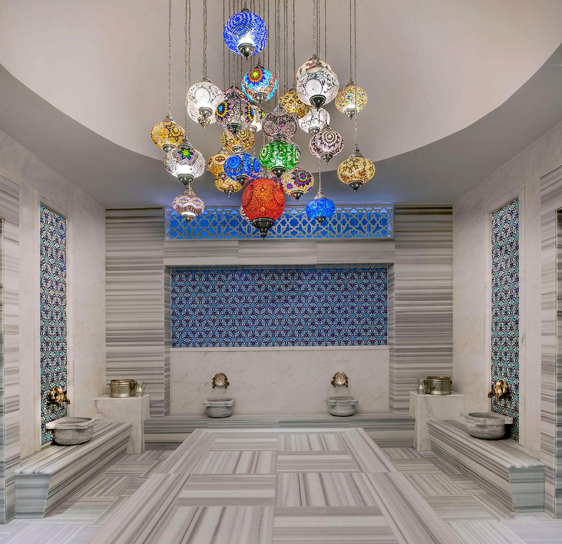 Innenansicht des Aska Lara Resort & Spa Hammam mit farbigen Lampen und Marmorboden.