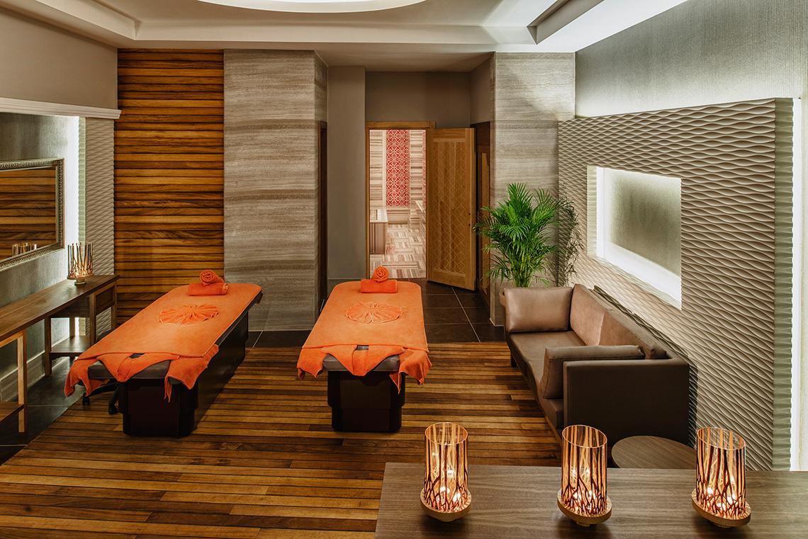 Wellness-Bereich im Aska Lara Resort & Spa mit zwei Behandlungstischen, einem Sofa und Pflanzen.