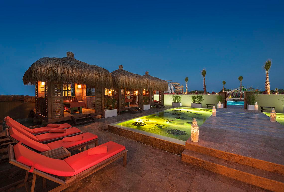 Nachtansicht der Terrasse im Aska Lara Resort & Spa mit beleuchteten Loungestühlen und einem kleinen Pool.