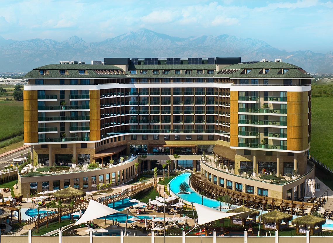 Außenansicht des Aska Lara Resort & Spa mit Swimmingpools und Bergen im Hintergrund.