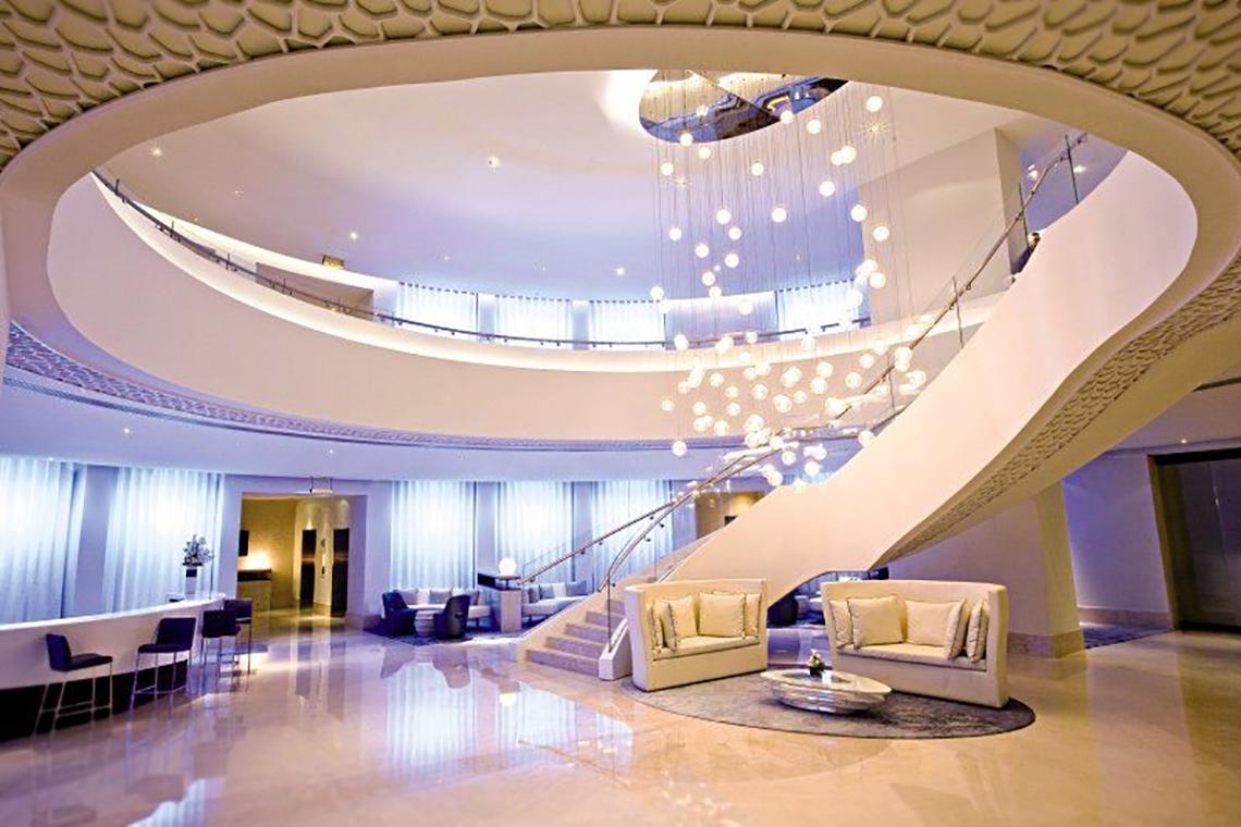 Lobby des JA Ocean View Hotels mit weißer Treppe, modernen Möbeln und einer zentralen Lichtinstallation.