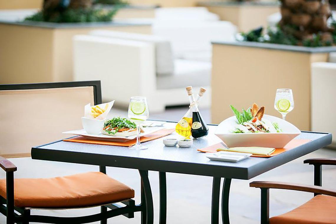 Gedeckter Tisch auf der Terrasse des JA Ocean View Hotels mit Salat, Öl und Getränken.