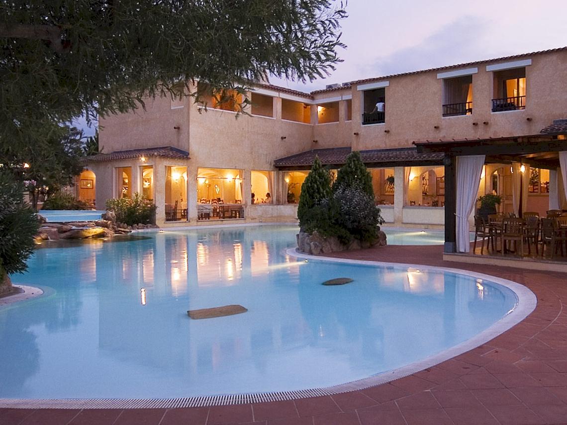 Abendansicht des Colonna Hotel Du Golf mit Swimmingpool und Außenbereich mit Tischen und Stühlen.