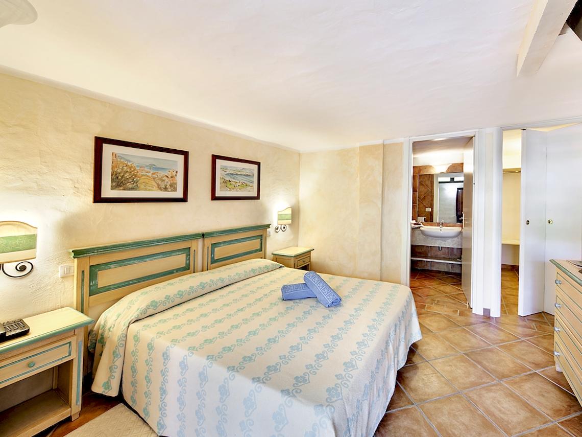Schlafzimmer im Colonna Hotel Du Golf mit zwei Nachttischen, einem Bett, zwei Gemälden und einem Badezimmer.