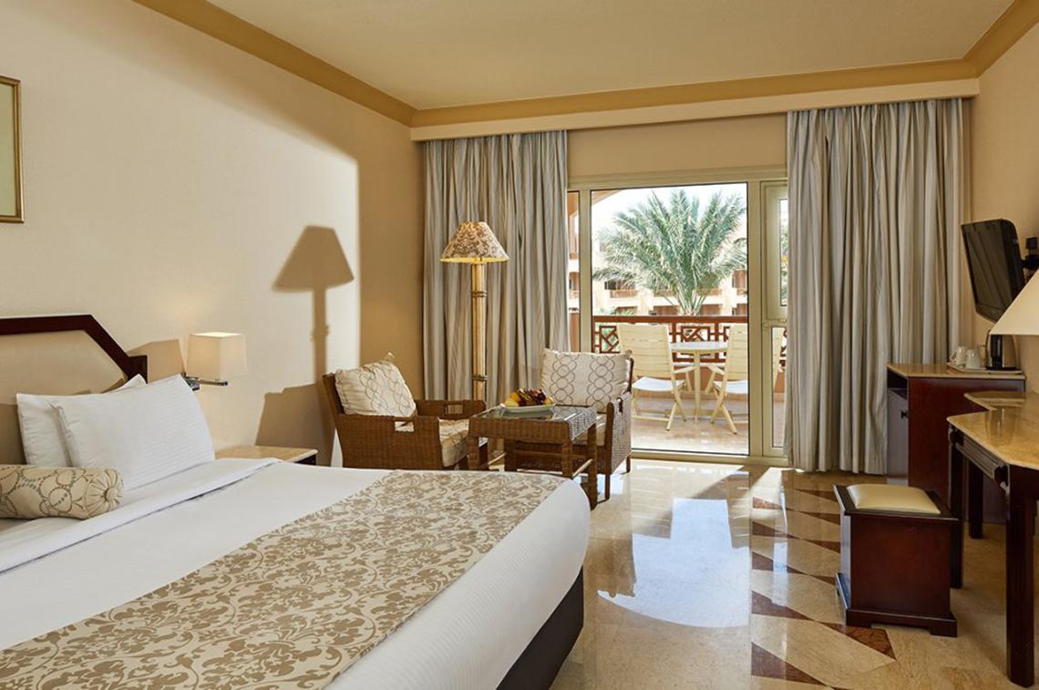 Luxuriöses Hotelzimmer im Continental Hotel Hurghada mit Balkon, bequemen Möbeln und Blick auf Palmen.