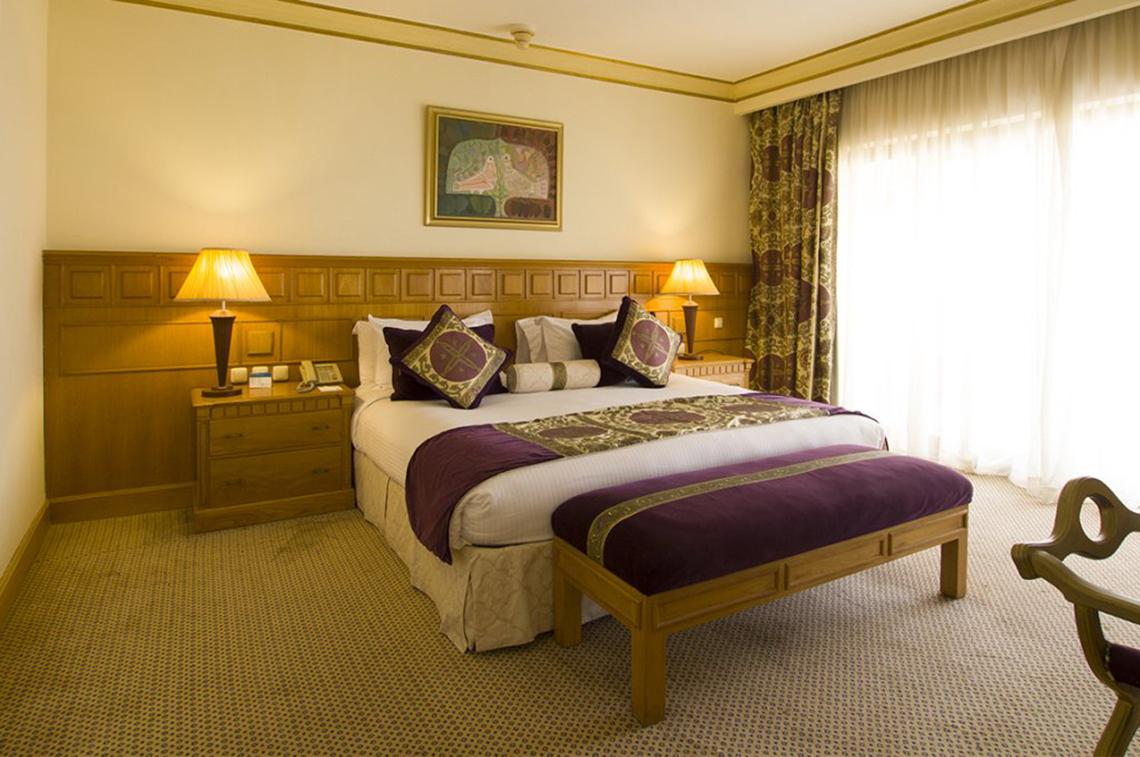 Schlafzimmer im Continental Hotel Hurghada mit großem Bett, Nachttischen, Lampen und Fenstervorhängen.