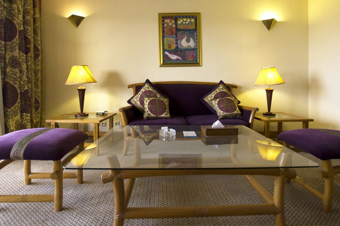 Wohnbereich im Continental Hotel Hurghada mit einem Glastisch, einem Sofa, Kissen, zwei Nachttischen und Lampen.