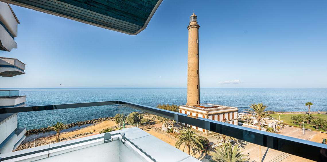Aussicht von einem Balkon auf einen Leuchtturm am Meer mit Gebäuden, Bäumen und Ozean