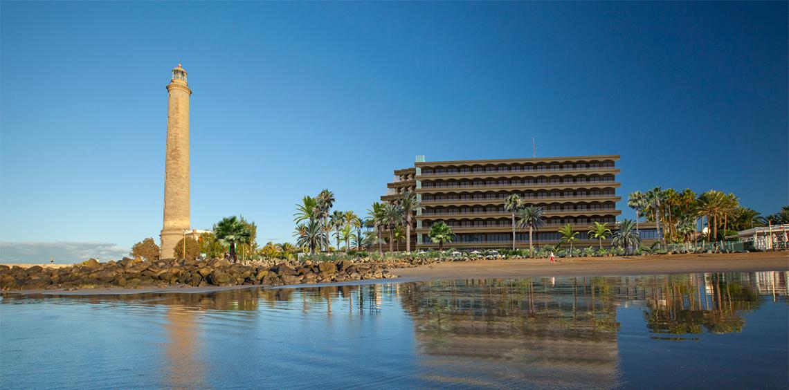 Außenansicht des Faro, a Lopesan Collection Hotel mit Leuchtturm und Gebäude am Strand