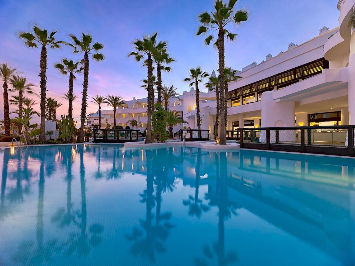 Außenpool des H10 Estepona Palace Hotels mit Palmen und weißem Gebäude im Hintergrund