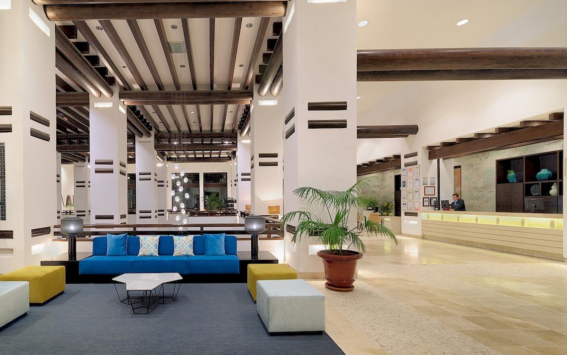 Lobby des H10 Estepona Palace mit blauer Couch, gelben Hockern und Empfangstresen