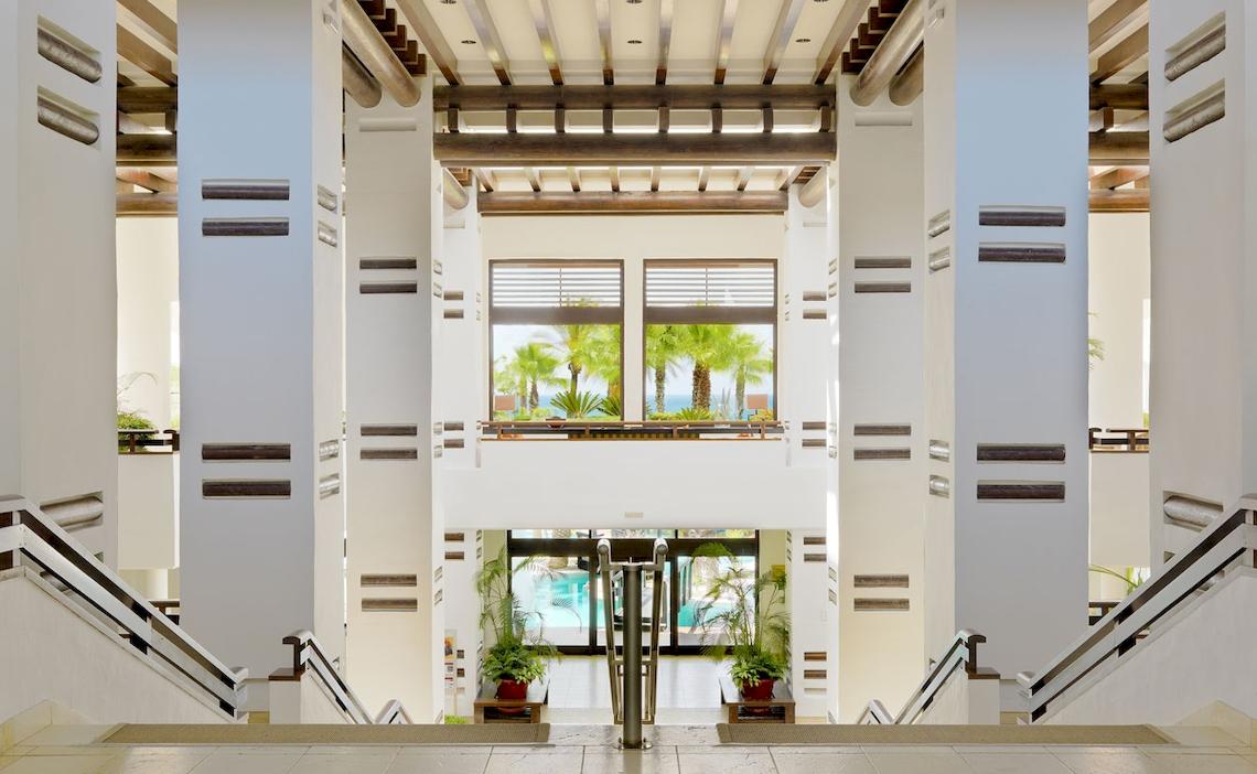 Innenansicht der Lobby im H10 Estepona Palace mit hohen Säulen und Glasfenstern.