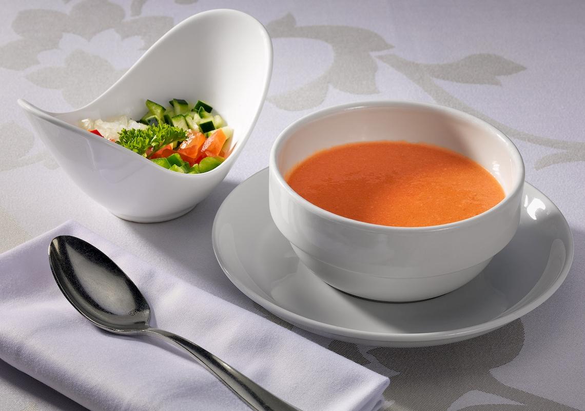 Ein weißer Teller mit einer weißen Schüssel Tomatensuppe und Salat.