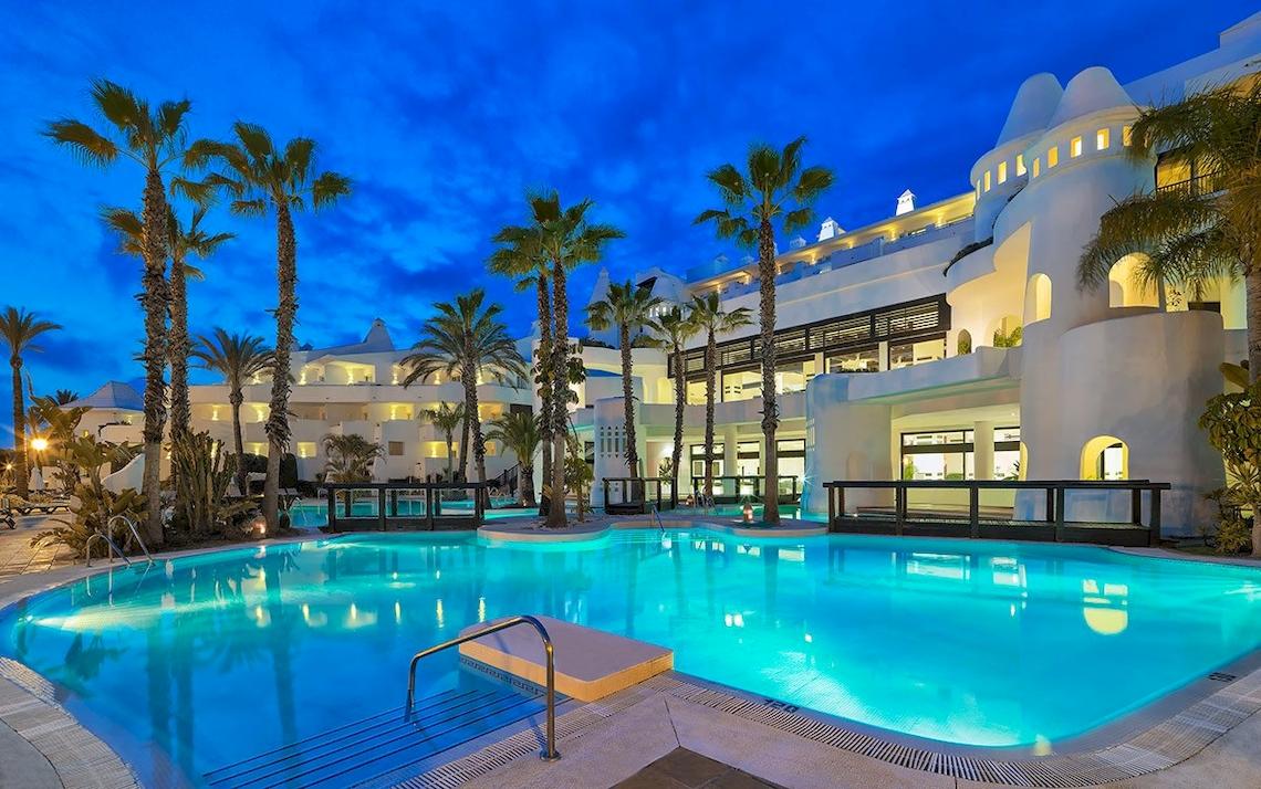 Außenpool des H10 Estepona Palace bei Nacht mit beleuchtetem Hotelgebäude und Palmen.