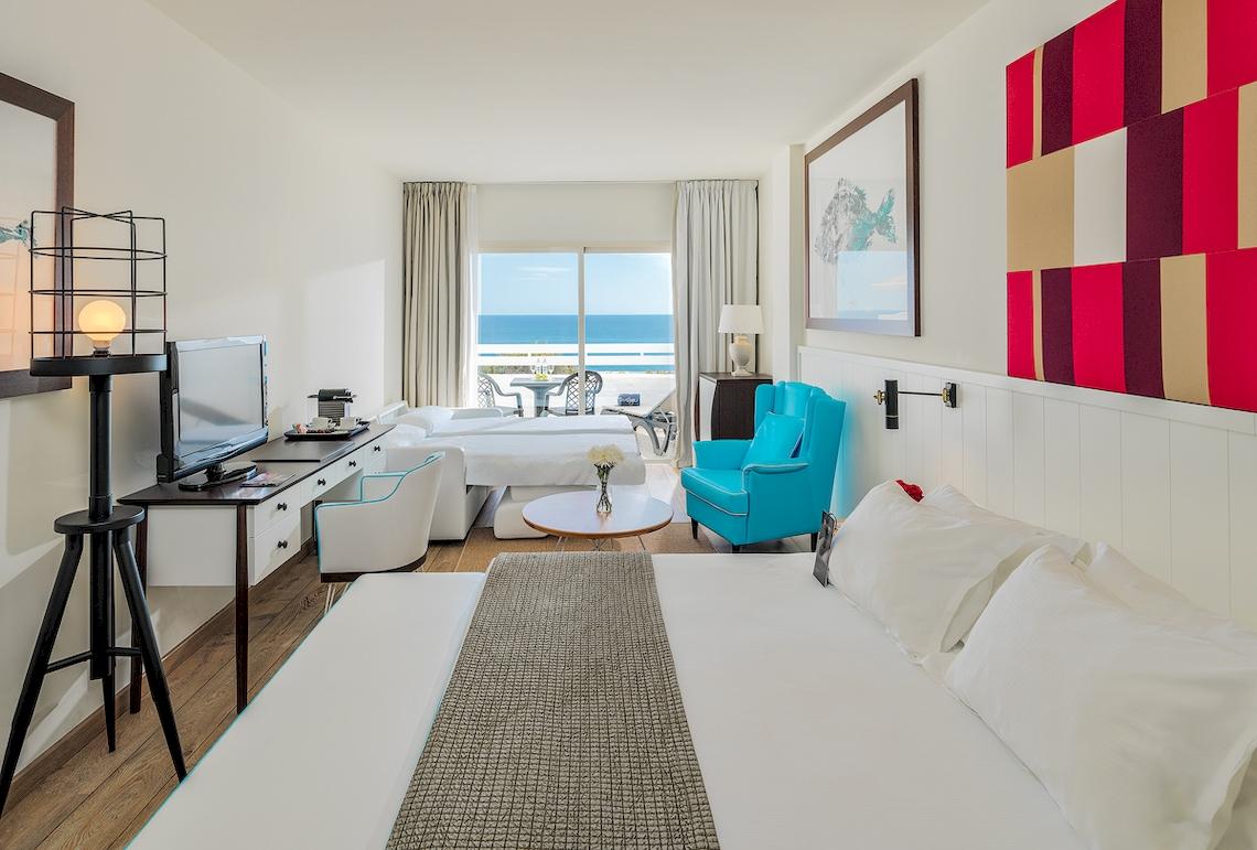 Hotelzimmer des H10 Estepona Palace mit Meerblick, zwei Betten, einem Schreibtisch und einem blauen Stuhl.