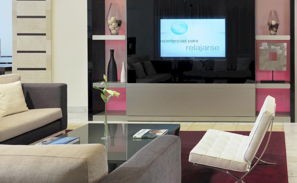 Wohnbereich des H10 Estepona Palace Hotels mit einem Fernseher, einem Tisch und einem Stuhl.