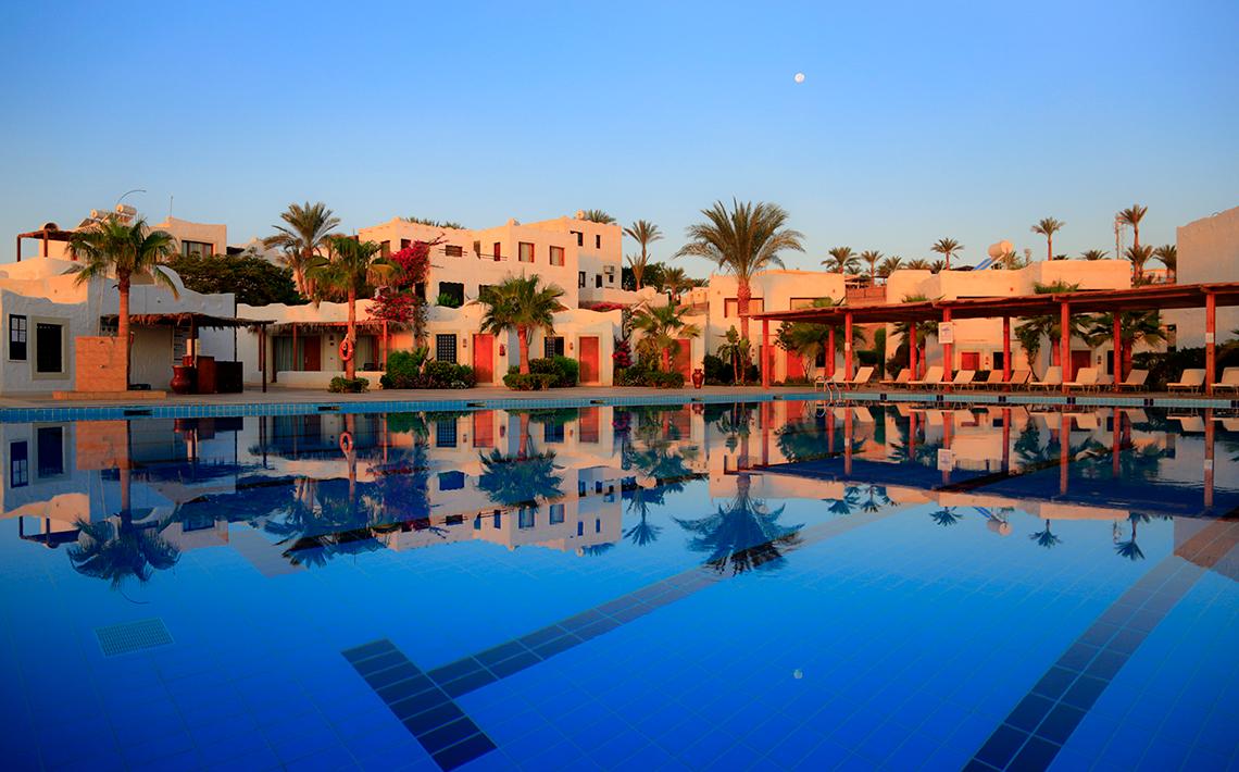 Außenpool des Sharm Club Beach Resort mit weißen Gebäuden und Palmen im Hintergrund.