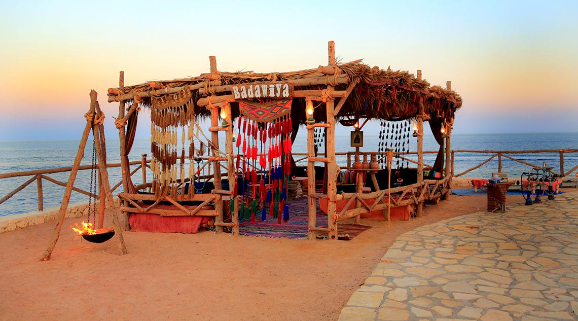 Abendstimmung am Sharm Club Beach Resort mit Blick auf das Meer und einem brennenden Feuer in einer kleinen Hütte.