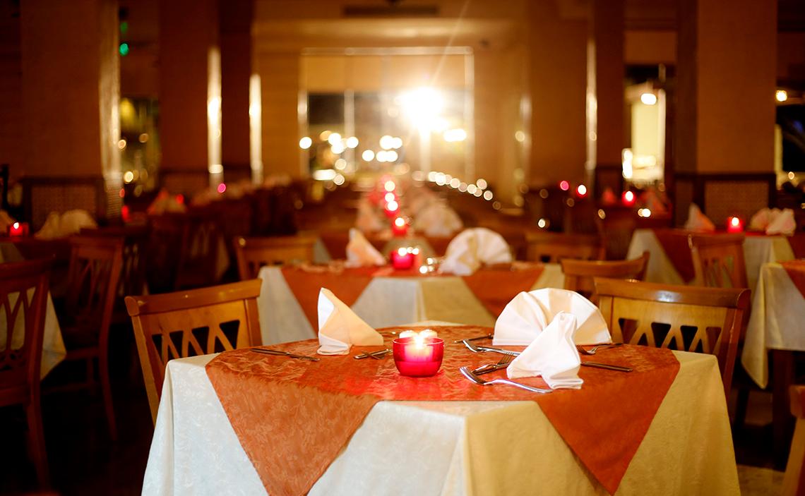 Ein Restaurant im Sharm Club Beach Resort mit gedeckten Tischen, roten Kerzen und dekorativen Lichtern.