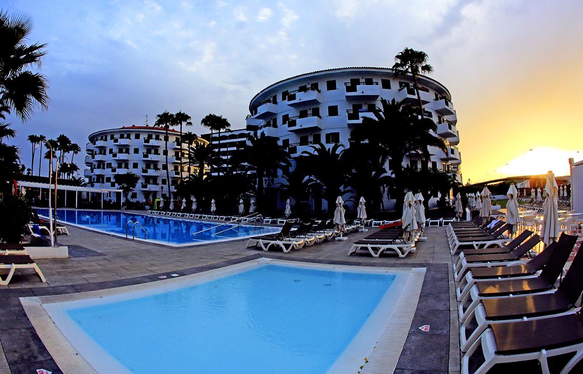 Poolbereich des Servatur Playa Bonita mit Liegestühlen und Palmen bei Sonnenuntergang