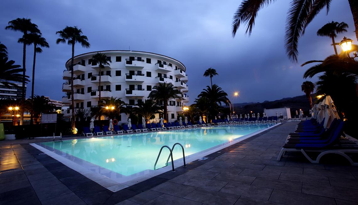 Poolbereich mit Liegestuehlen und Palmen vor dem Hotel Servatur Playa Bonita bei Abenddämmerung