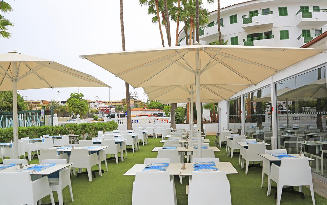 Terrassenbereich des Restaurants im Servatur Playa Bonita mit weißen Tischen und Stühlen unter Sonnenschirmen