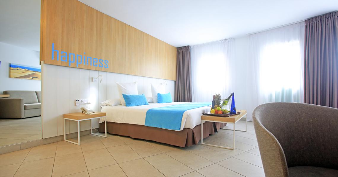Hotelzimmer mit einem Bett, blauem Überwurf und Dekorbottles auf einem Tablett