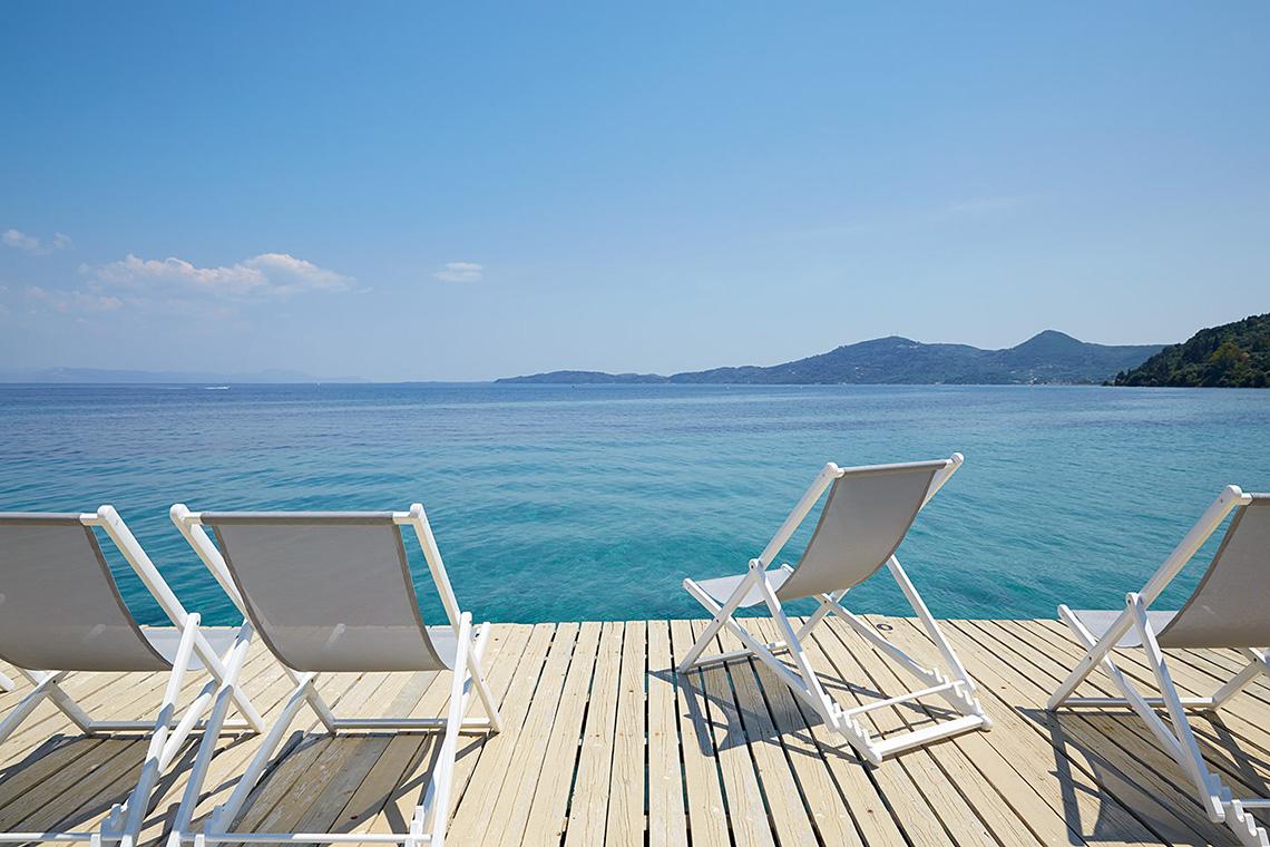 Vier weiße Sonnenliegen auf einer Terrasse mit Blick auf das Meer