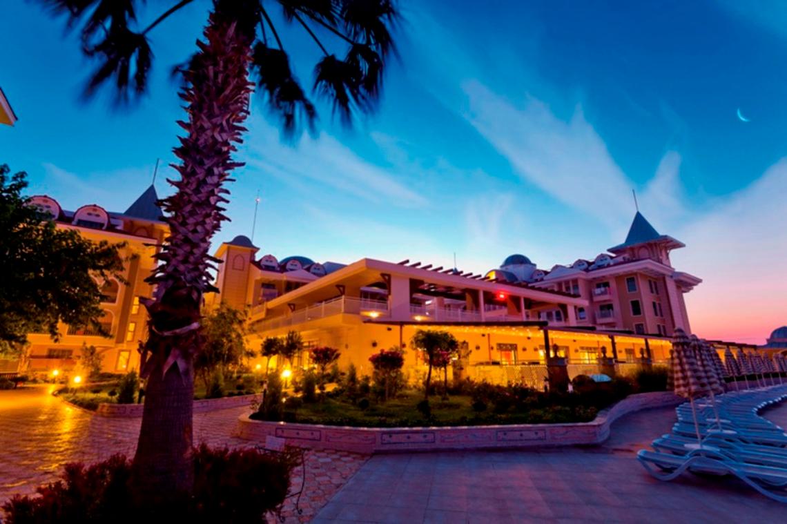 Abendlicher Blick auf das Side Star Resort Hotel mit leuchtenden Lichtern und einer Palme vor dem Gebäude.