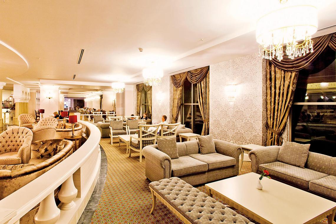 Lobby des Side Star Resort Hotels mit gepolsterten Sesseln und Sofas, Kristalllampen und einem Tisch mit einer roten Blume.
