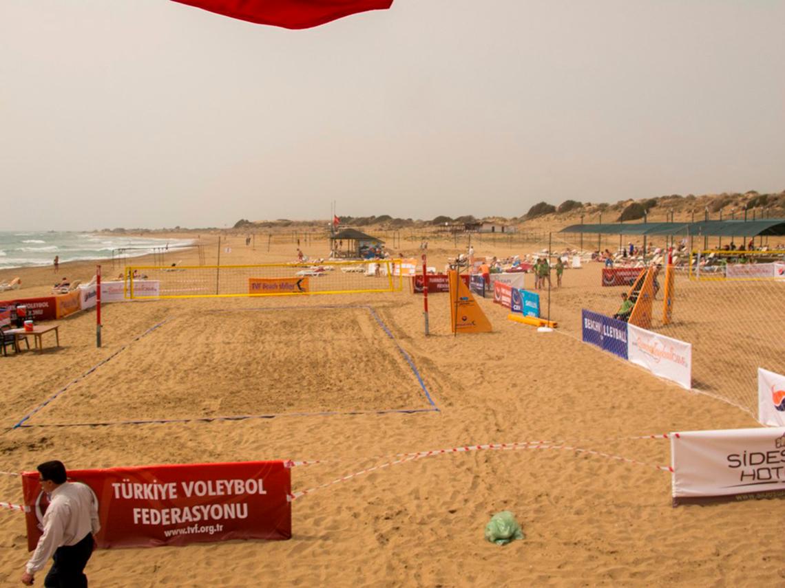 Ein Volleyballspielfeld am Strand mit Werbetafeln und einer Person, die darauf zugeht.