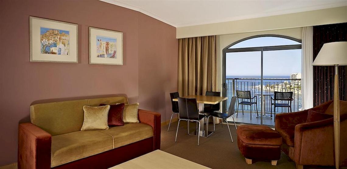 Hotelzimmer mit Meerblick, Sofa, Tisch, Stühle und Balkon.