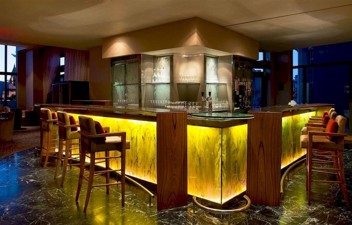 Die Bar im Malta Marriott Hotel mit gelben Beleuchtung und Holzstühlen.