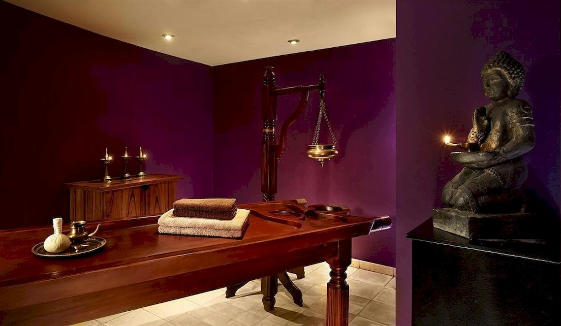 Behandlungsraum im Malta Marriott Hotel & Spa mit violetten Wänden, Buddha-Statue, Tisch und Kerzen