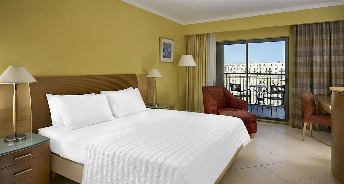 Hotelzimmer mit Balkon im Malta Marriott Hotel & Spa, mit gelben Wänden, bequemem Bett und Ausblick auf die Stadt.