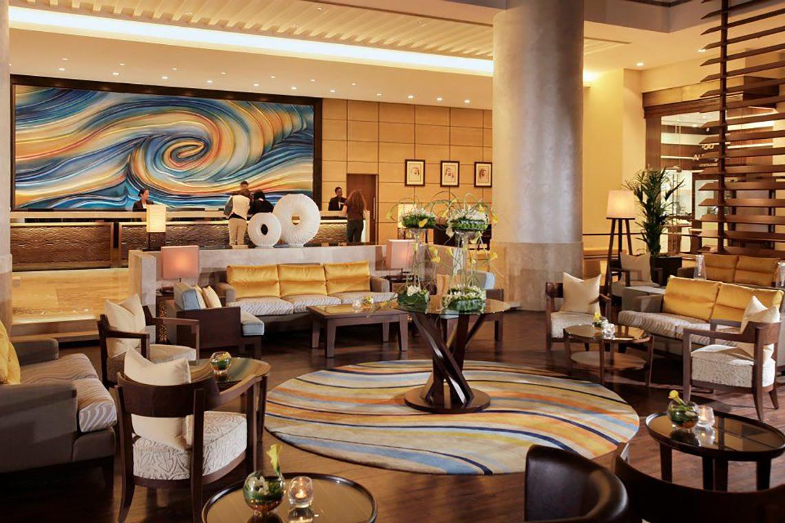 Lobby des Amwaj Rotana Hotels mit großen Wandbild, Sofas und Tischen.