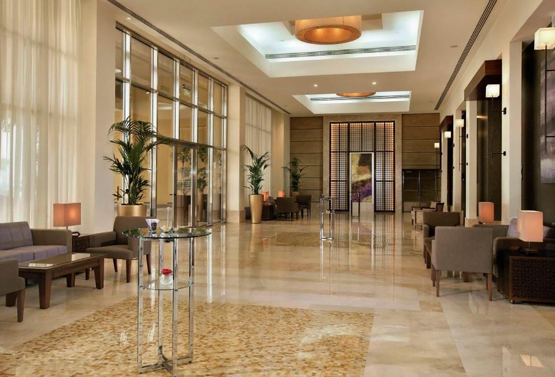 Lobby des Amwaj Rotana Hotels mit modernen Möbeln, großen Fenstern und Pflanzen.