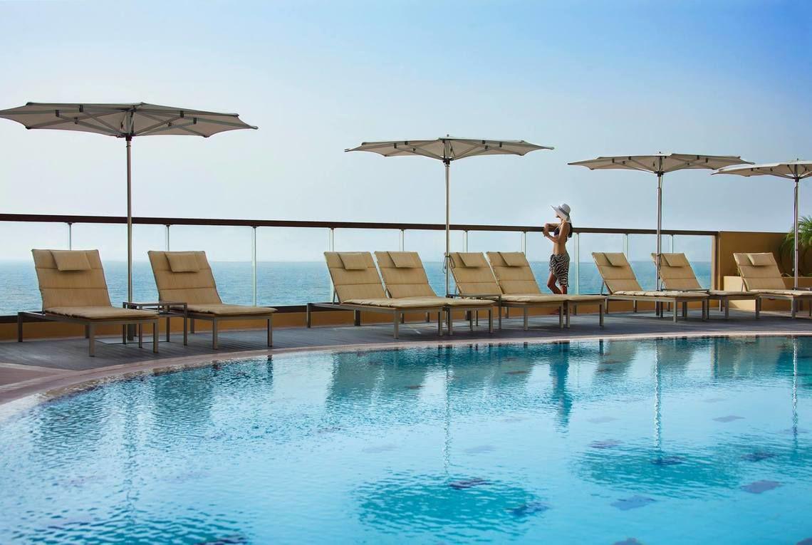 Pool mit Liegen und Sonnenschirmen im Amwaj Rotana Hotel mit Blick auf den Ozean