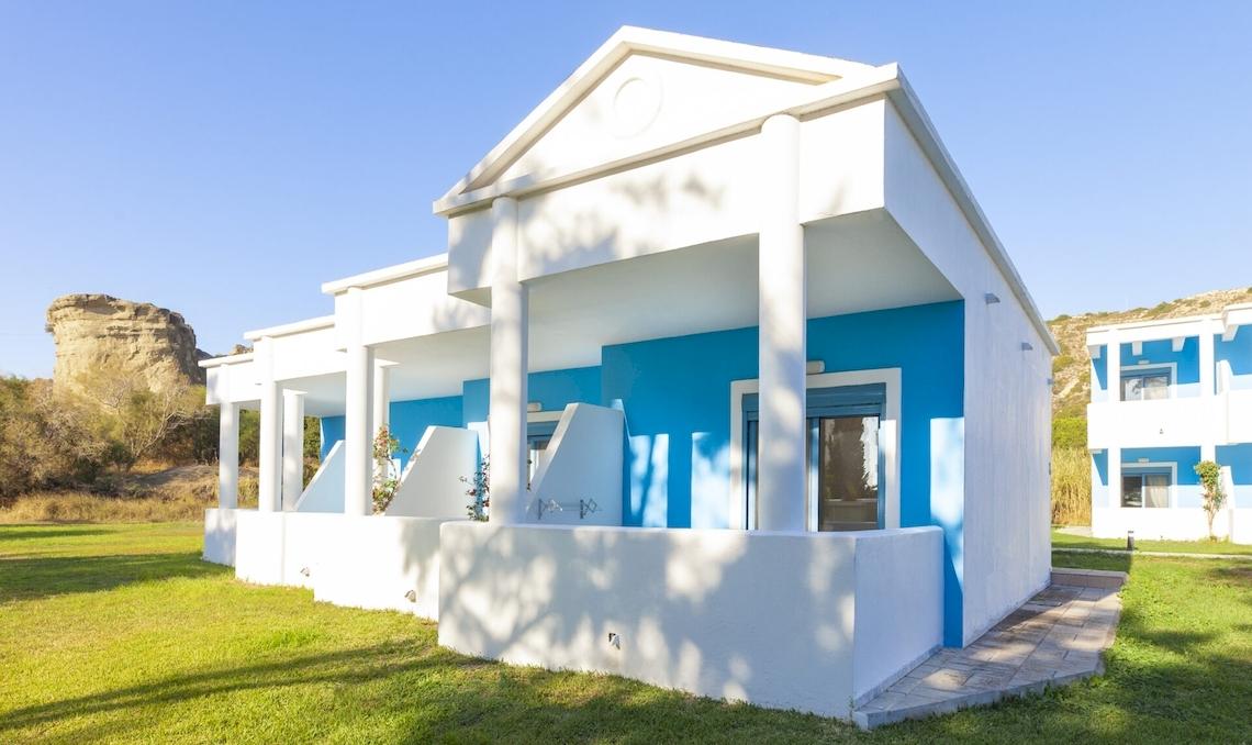 Außenansicht des Blue Sea Beach Resorts mit weißen und blauen Wänden und grüner Rasenfläche.