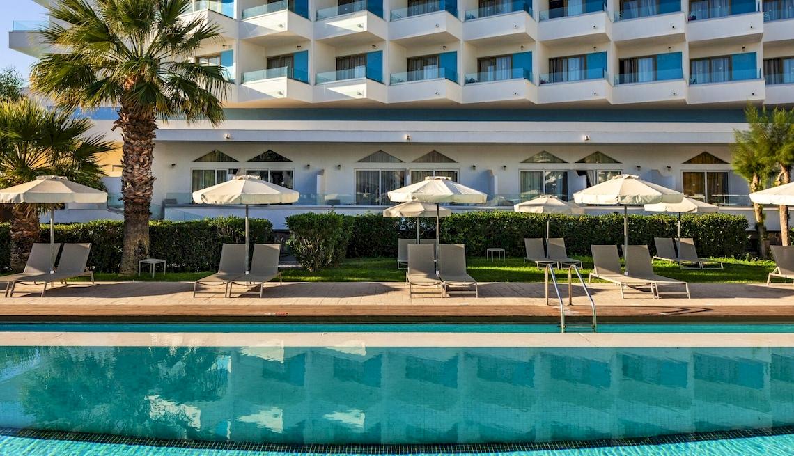Außenbereich des Blue Sea Beach Resorts mit Swimmingpool, Sonnenliegen und Sonnenschirmen.