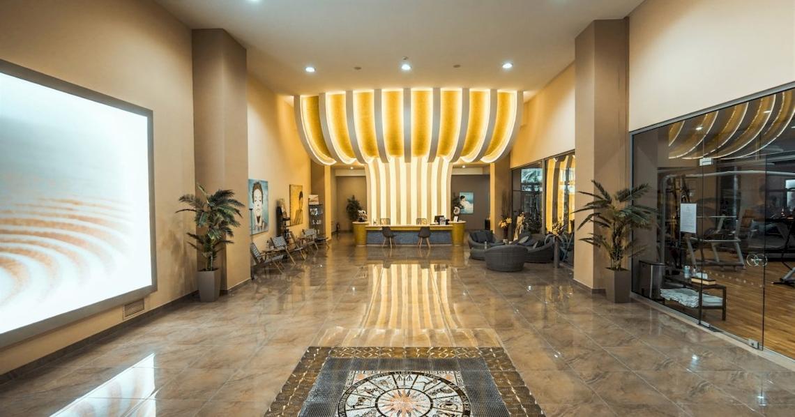 Ein Hotelfoyer mit einer großen Empfangshalle, gelben Leuchten und Pflanzen.
