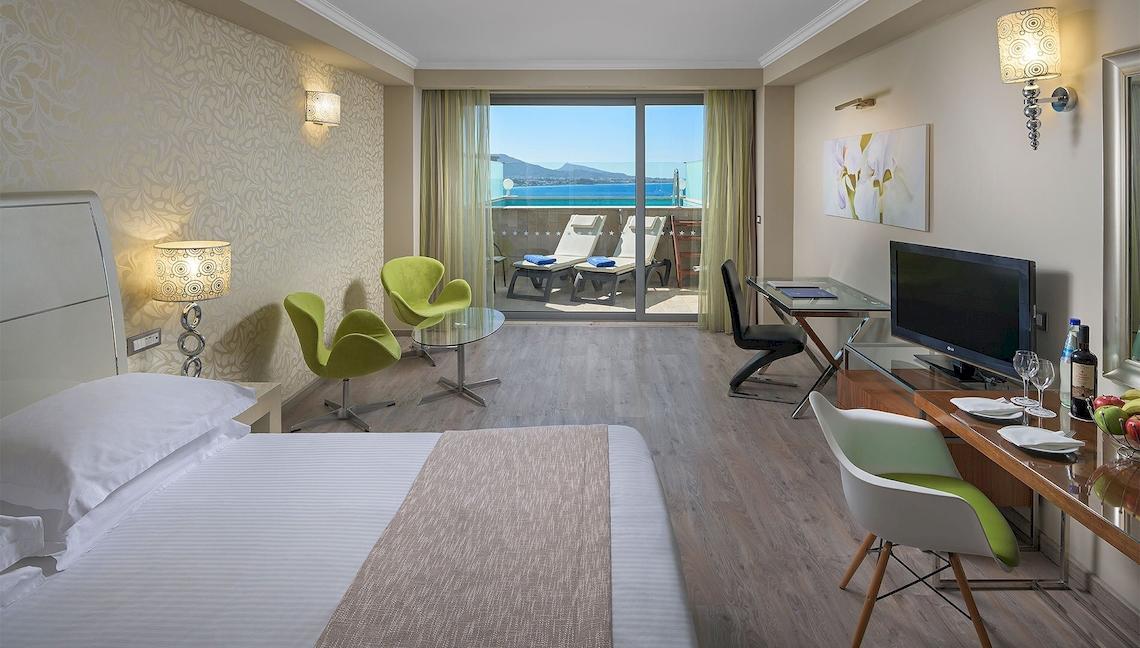 Innenansicht eines Hotelzimmers im Atrium Platinum Luxury Resort Hotel & Spa mit Balkon, Fernseher und Schreibtisch.