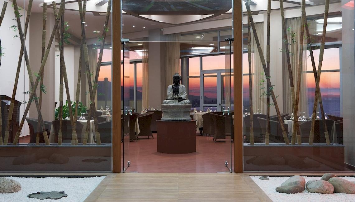 Innenansicht des Atrium Platinum Luxury Resort Hotel & Spa Restaurant mit Buddha-Statue und Glaswänden.