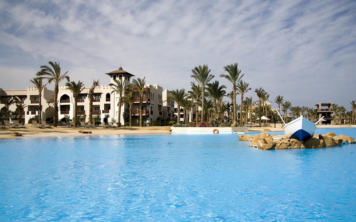 Ein Swimmingpool des PickAlbatros Sands Port Ghalib Hotels mit einem Boot im Hintergrund und Palmen.