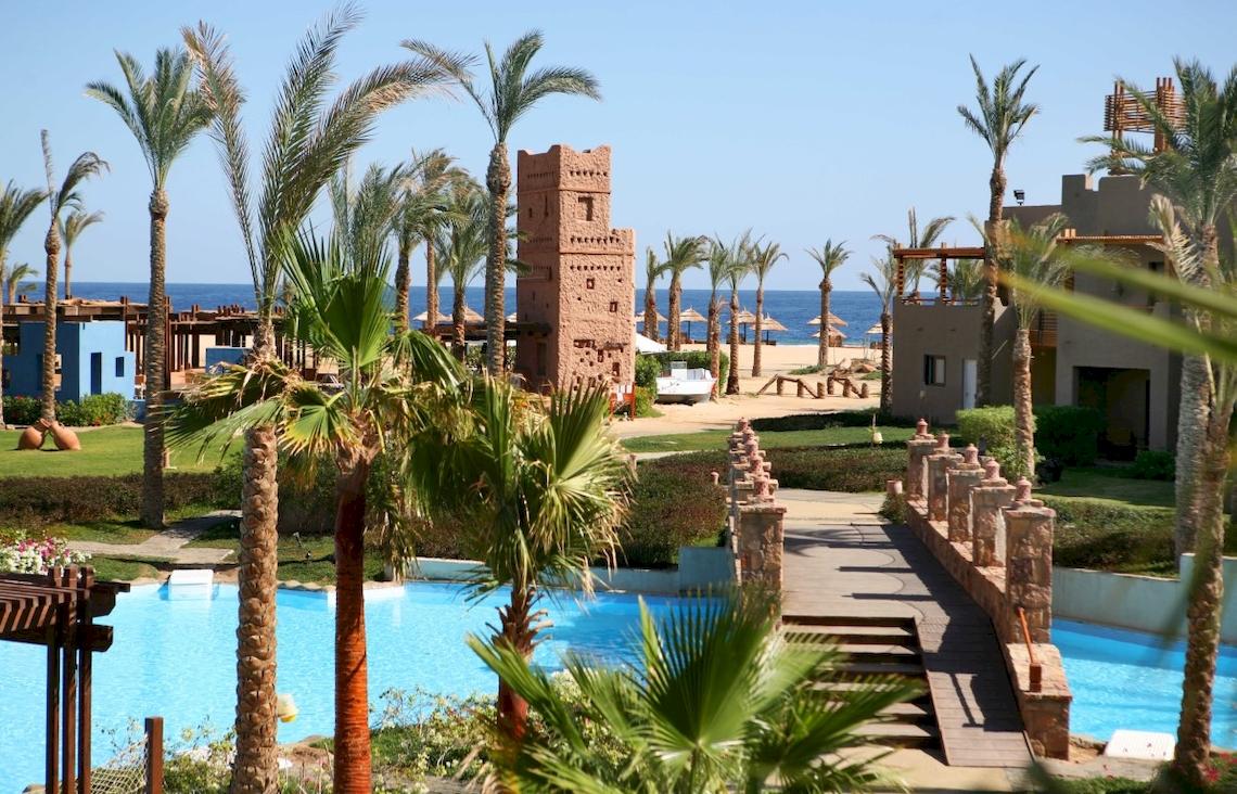 Außenbereich des PickAlbatros Sands Port Ghalib Hotels mit Swimmingpool, Palmen und Gebäuden.