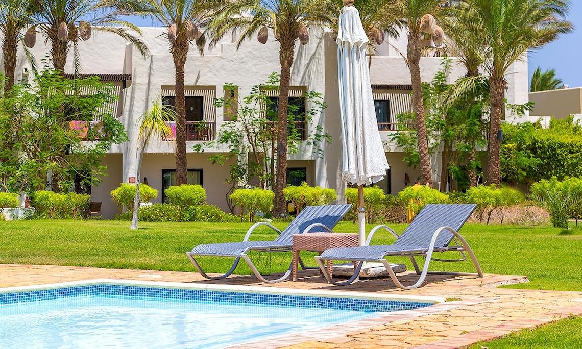 Pool mit Liegestühlen und Sonnenschirm vor einem Hotel